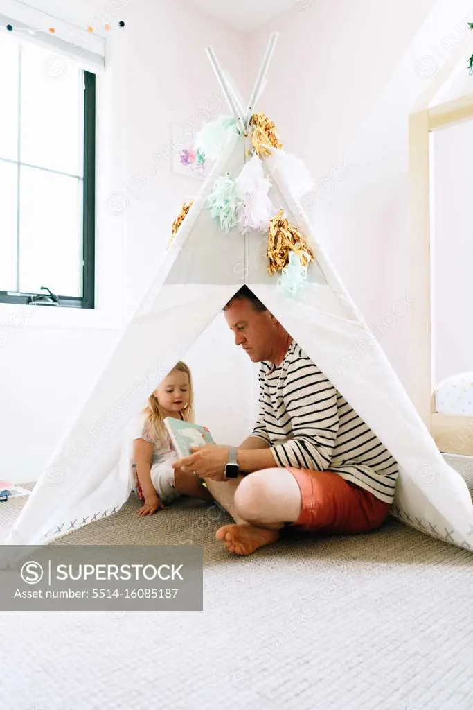 Portrait of a father and daughter reading together in a play tipi