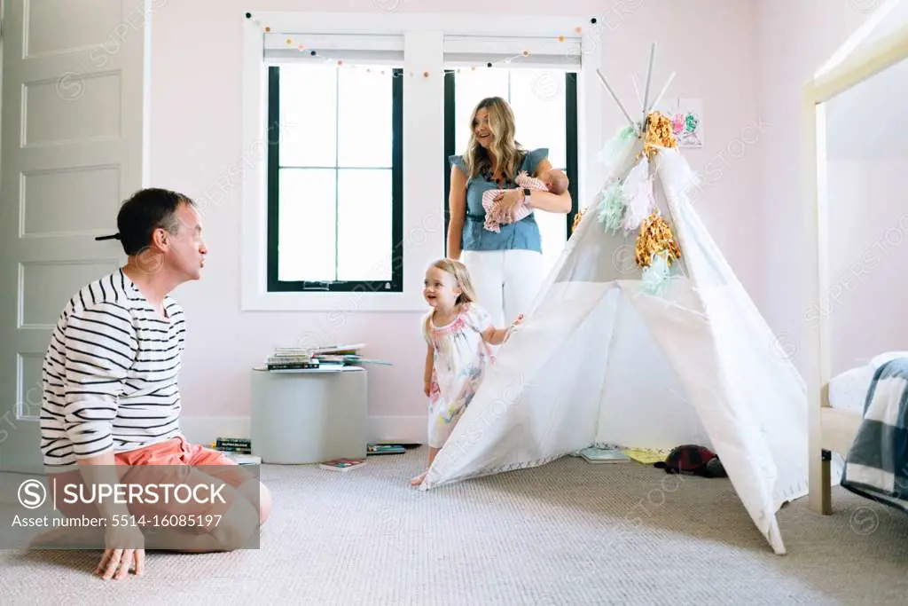A family of four play together in a child's room with a modern tipi