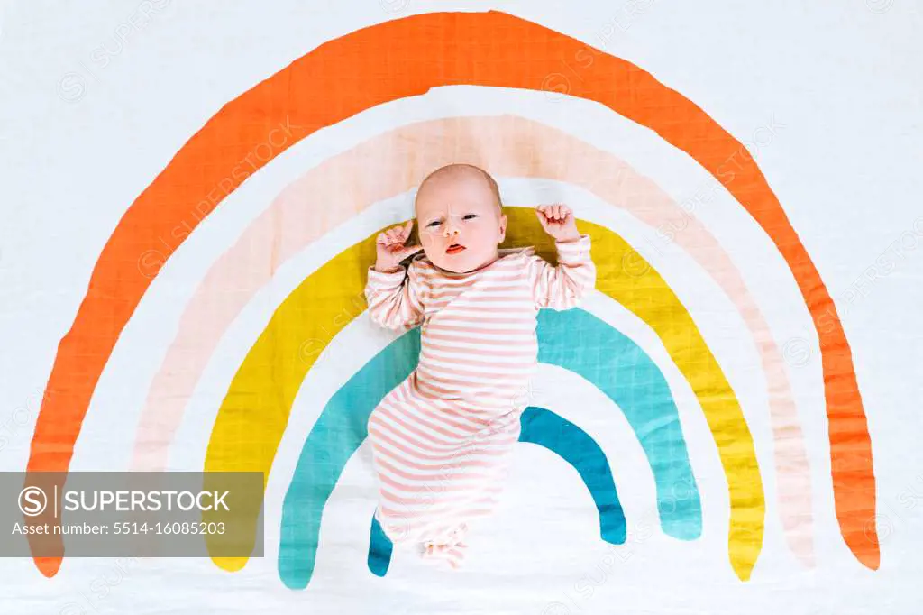 A newborn baby girl lying on a rainbow painted blanket