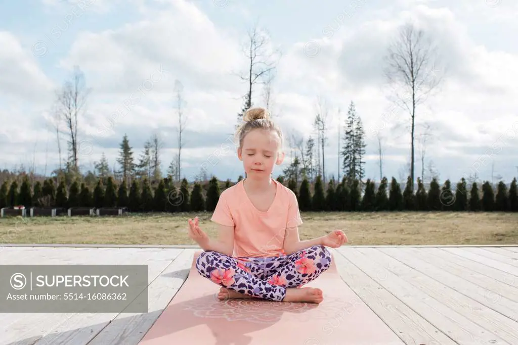 young girl meditating doing yoga in her back yard at home