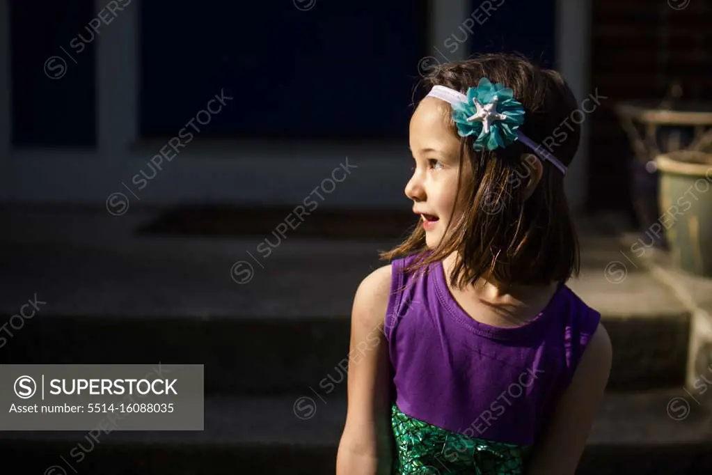 A beautiful little girl in a headband looks over her shoulder smiling