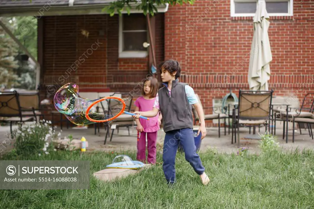 Two children create giant bubbles in yard with a bubble wand