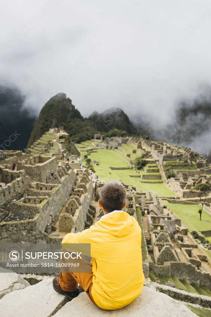 A man in a yellow jacket is sitting near ruins of Machu Picchu, Peru