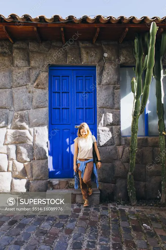 A young woman is standing near a blue old door in Cusco, Peru