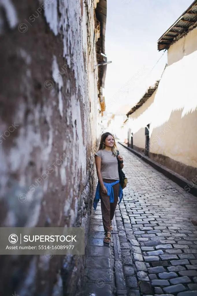 A young woman is standing near an old wall in Cusco, Peru