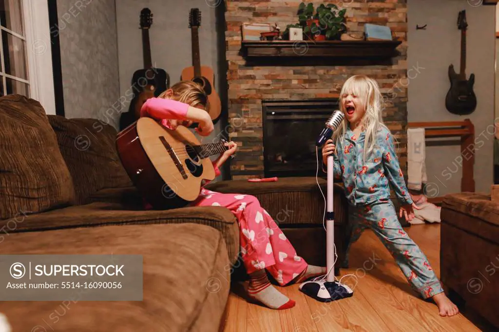 Young girls singing loudly and playing guitar in living room