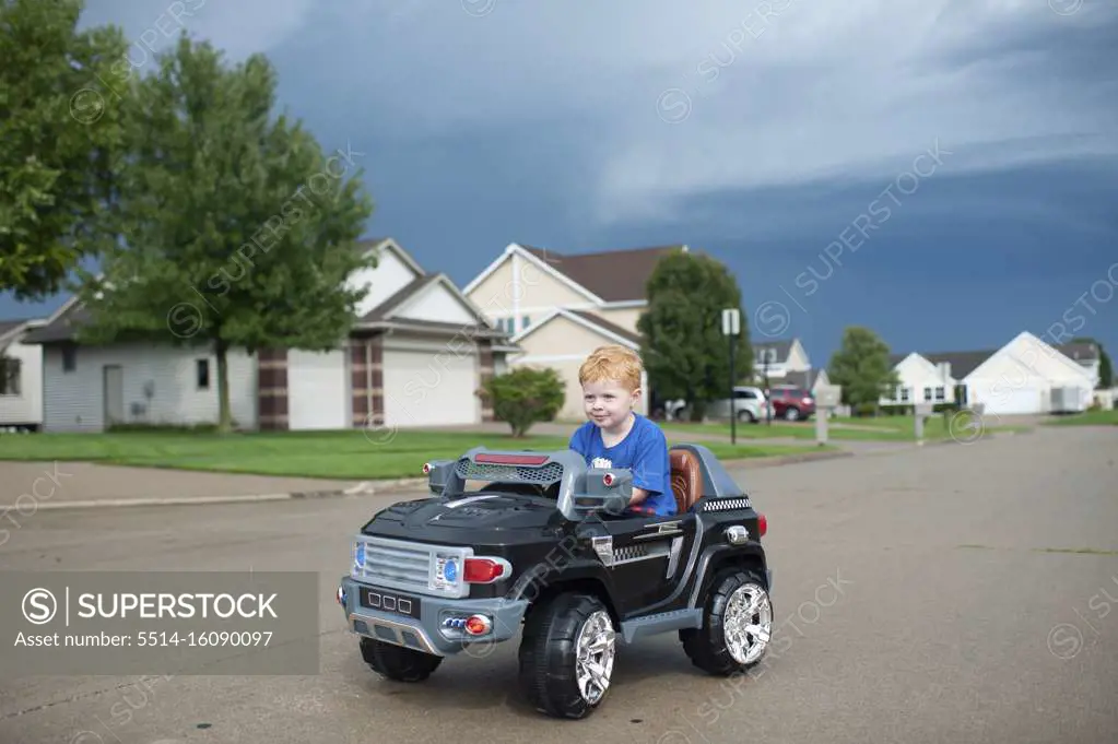 Young boy drives electric toy car down neighborhood street