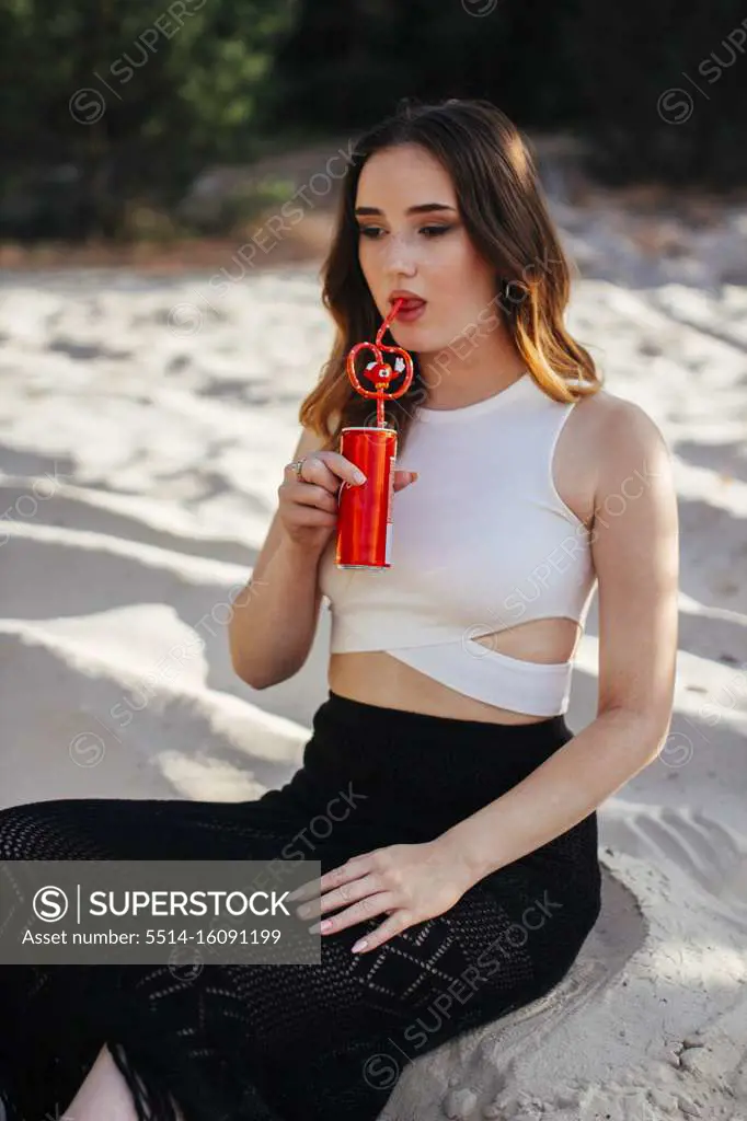 Woman drinking a drink from an iron can by taking a straw in her mouth