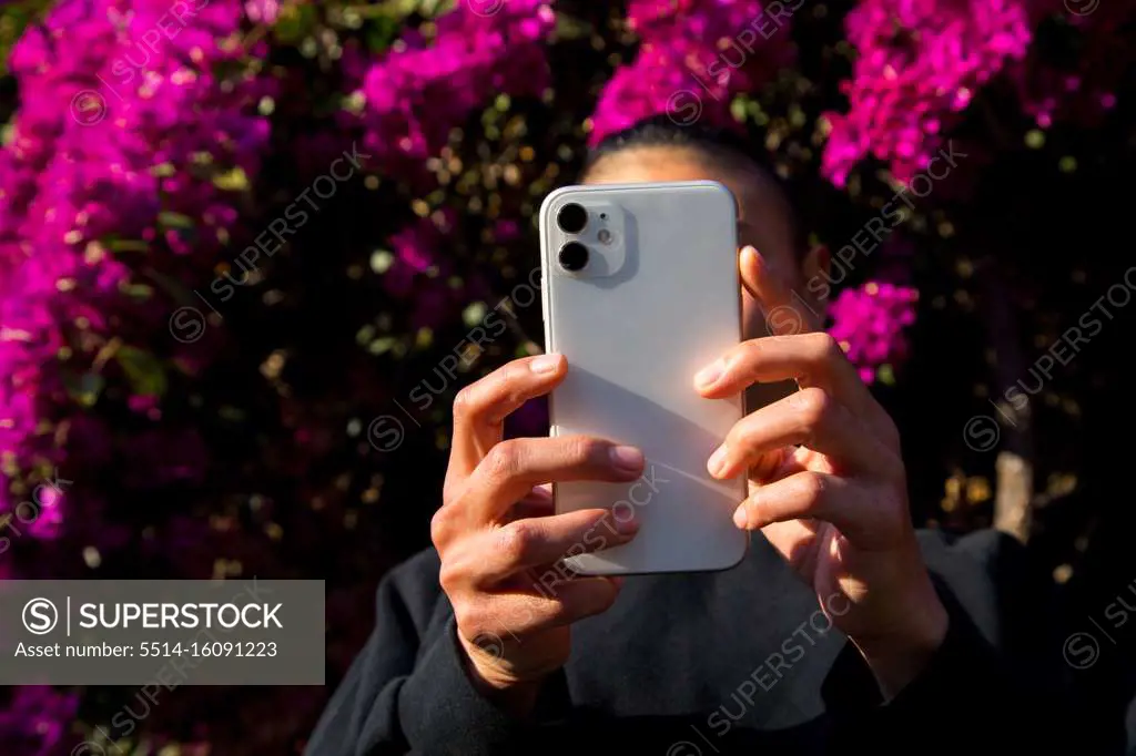 woman using cell phone outdoors in front of flower blossoms
