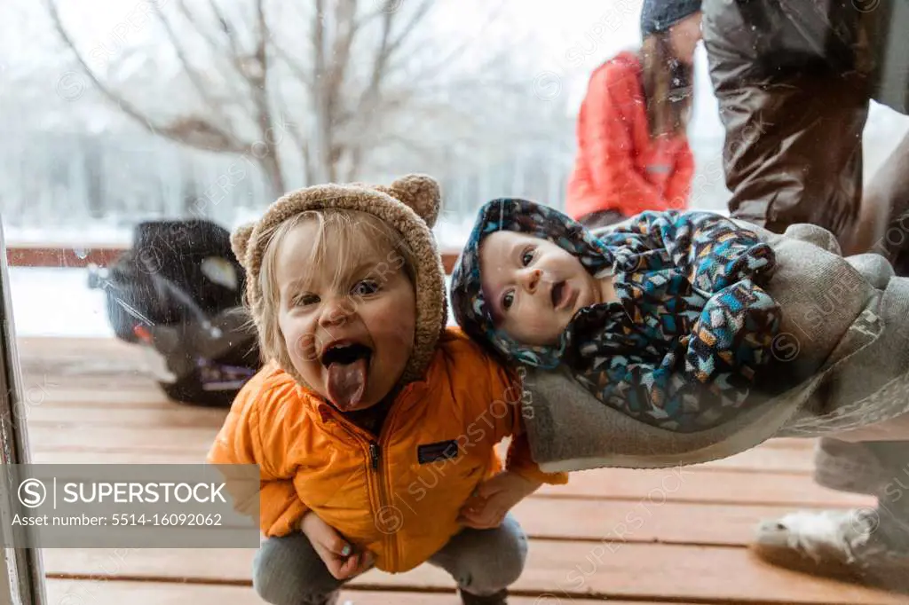 young kids smile and look through window at uncle during quarantine