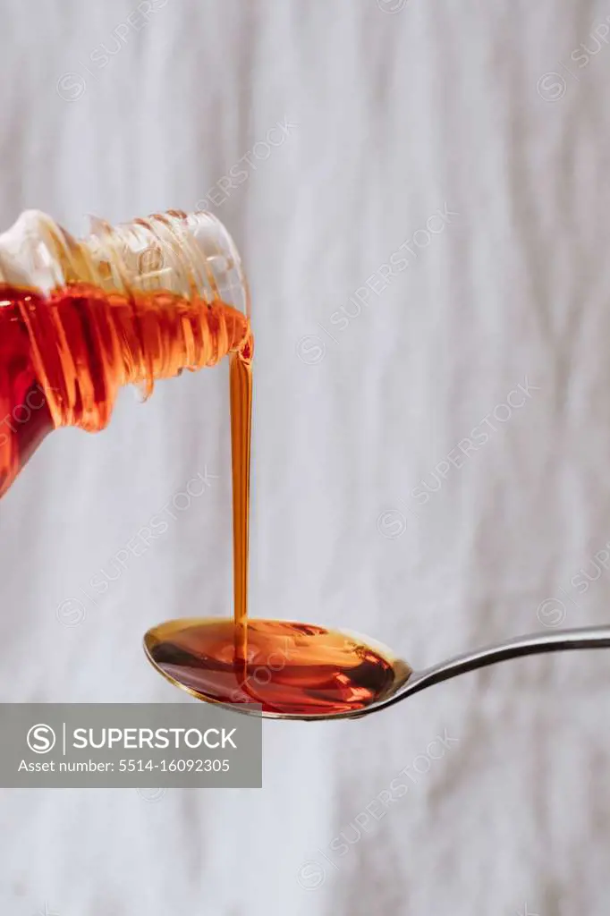 Bright orange liquid medicine being poured out onto a metal teaspoon