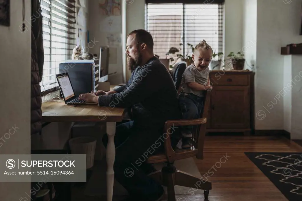 Dad working from home with one year old boy crying while he works