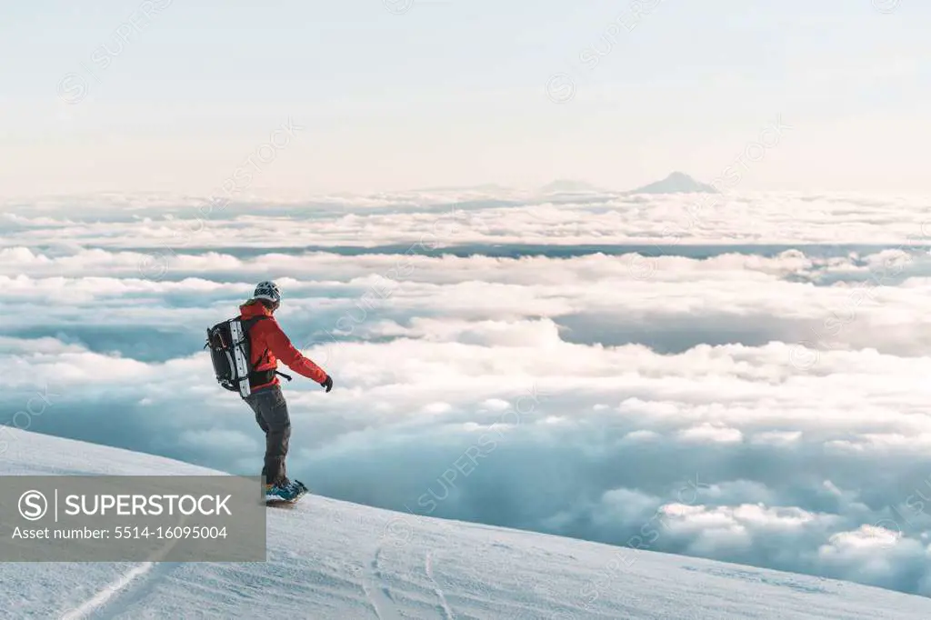 Snowboarder riding down mountain at sunset above clouds