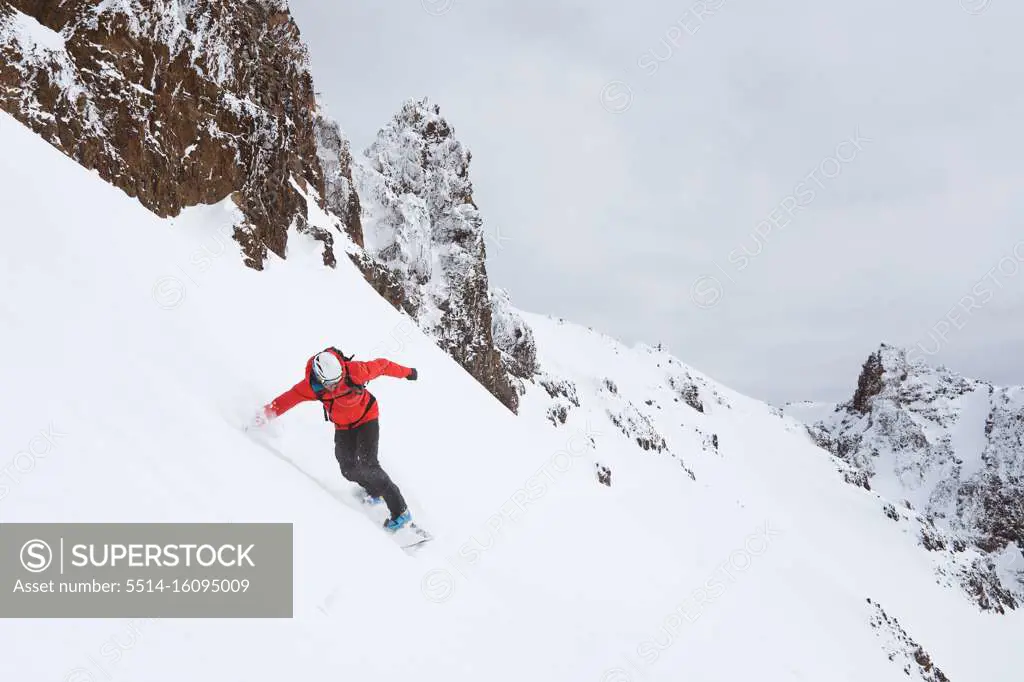 Snowboarder riding down mountain in red jacket