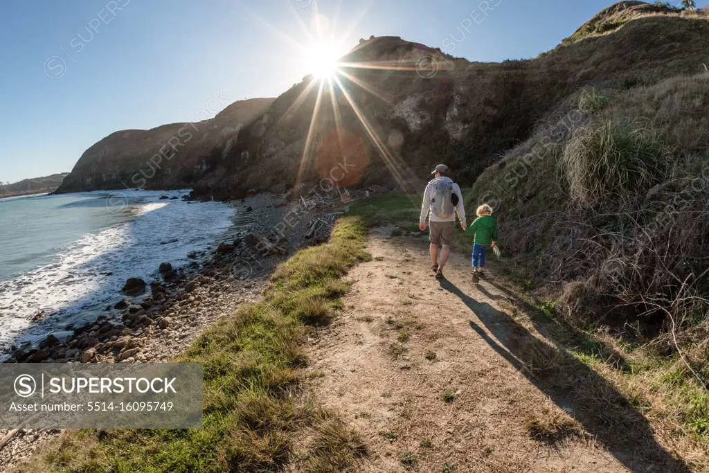 Dad and small child holding hands on path near ocean on a sunny day