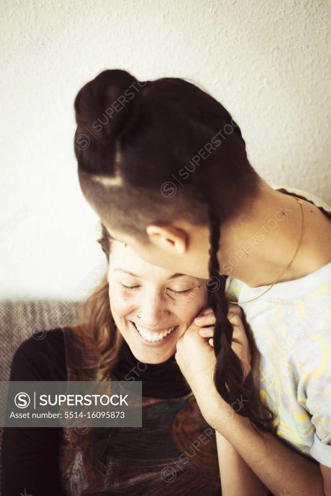 Same Sex Lesbian Couple Stay At Home And Cuddle Laughing In Warm Light