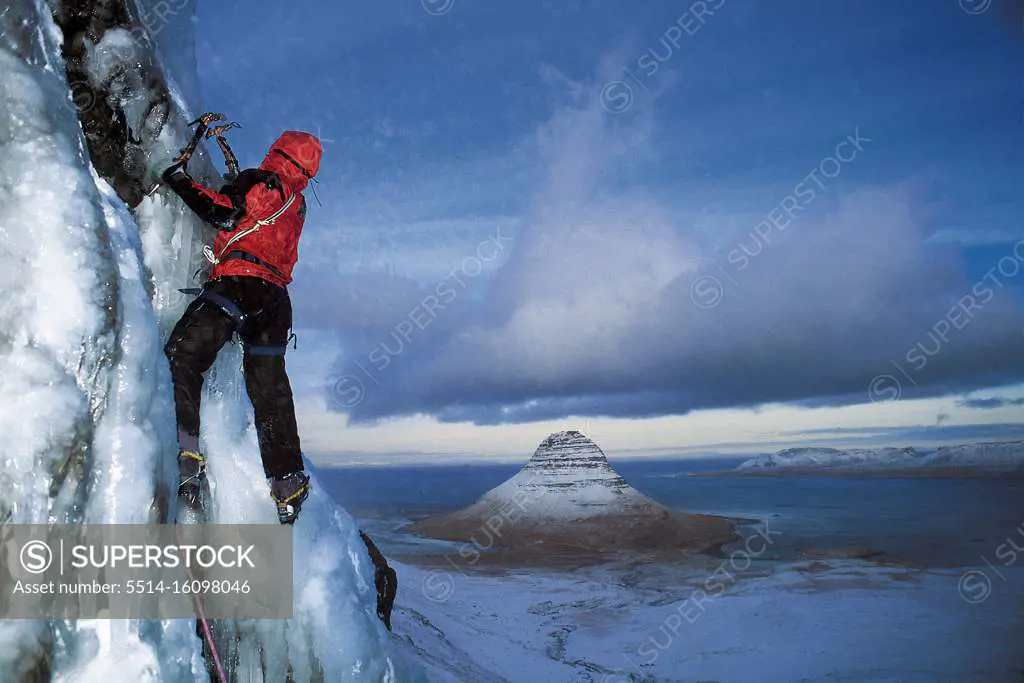 man climbs frozen waterfall above Grundafjordur fjord in Iceland