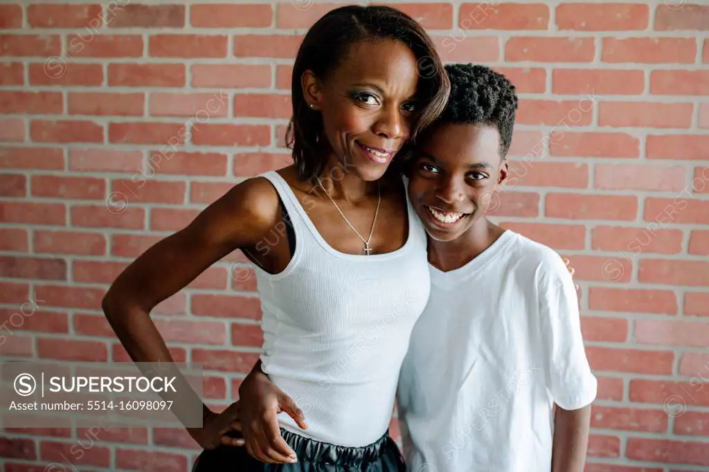 Pretty black mom hugging smiling preteen son in front of brick wall