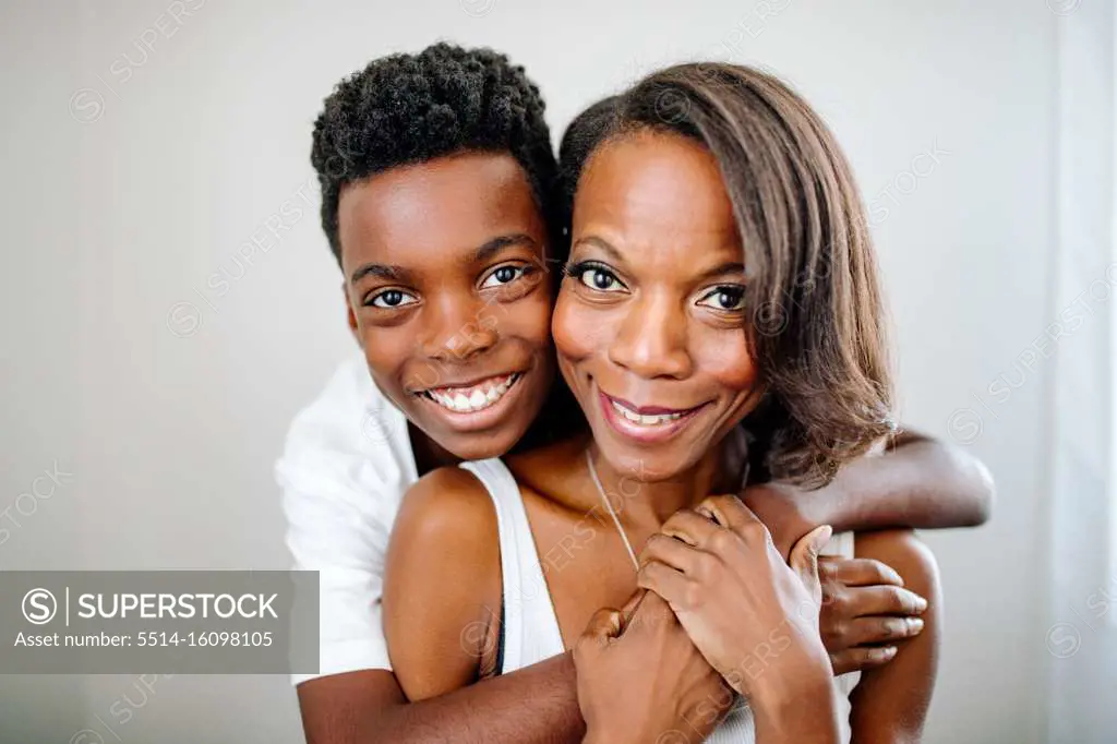 Handsome happy preteen black boy hugging beautiful mom from behind