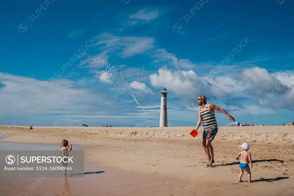 Kids playing with water at the beach with their dad on a sunny day