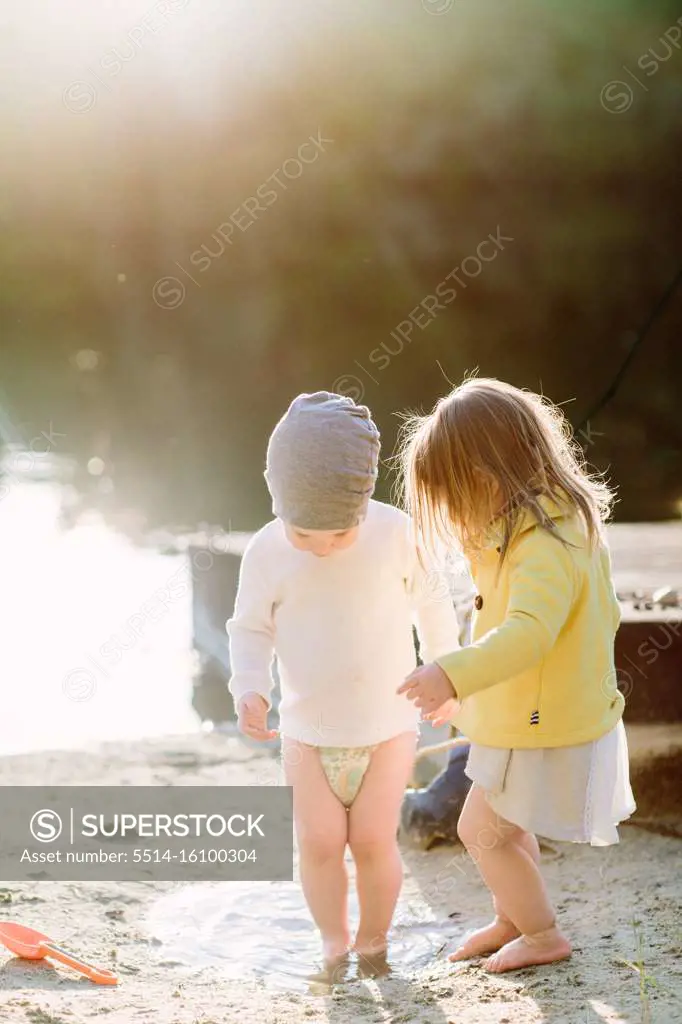 Toddlers stepping in a puddle at the beach in the sand during golden h