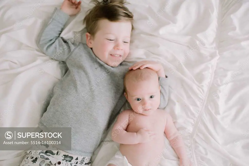 Big brother and baby sister lying on the bed from above