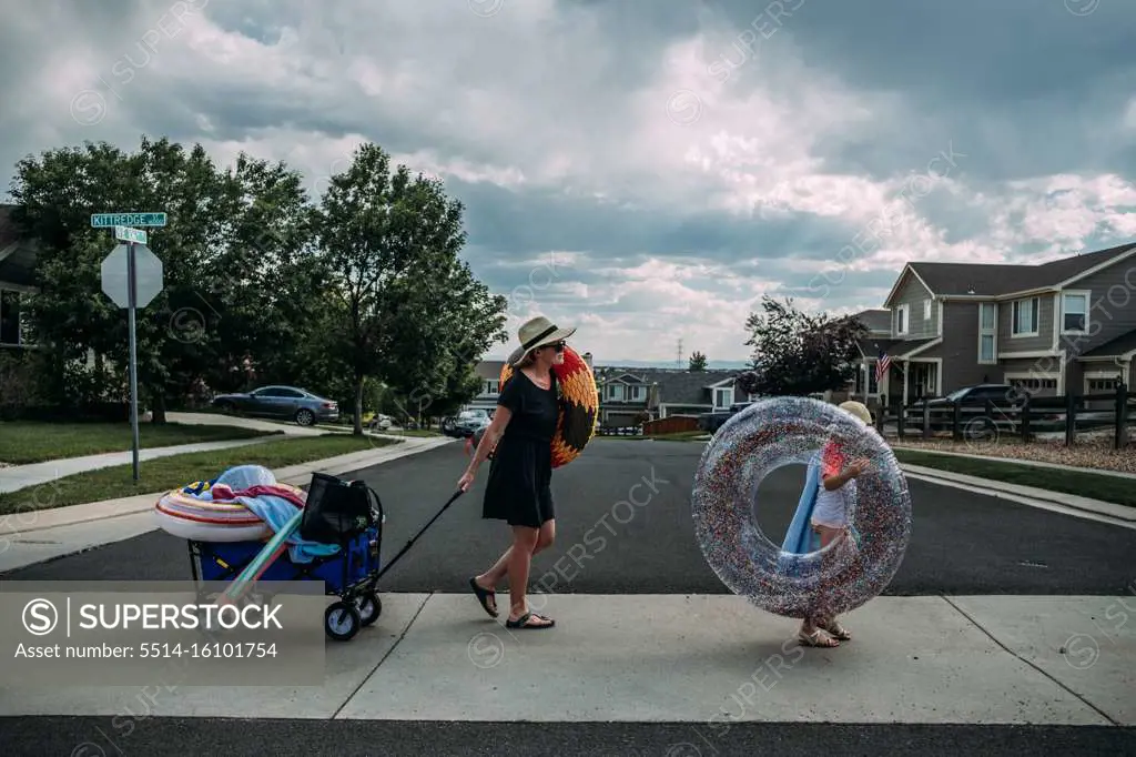 Mom walking with daughter carrying pool toys on summer day