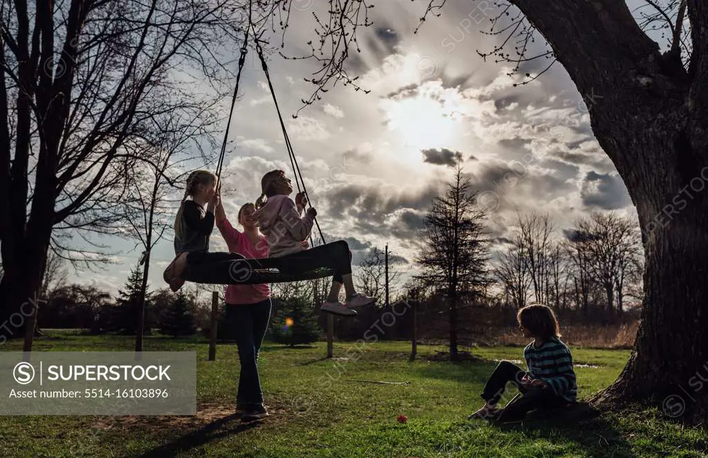 Children playing outside on a tire swing at sunset