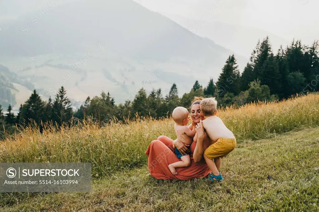 Children hugging their mother with mountains in the back in summer