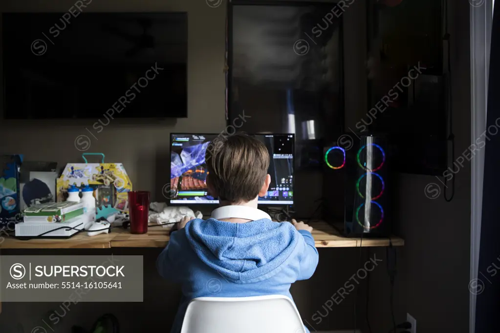 Rear View of Teen Boy Playing On Gaming Computer At Messy Desk