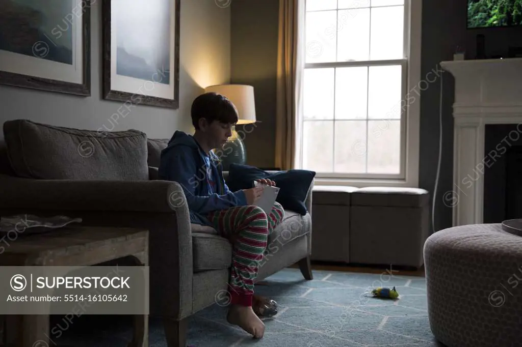 Side Silhouette of Teen Boy Sitting on Couch Opening A Letter