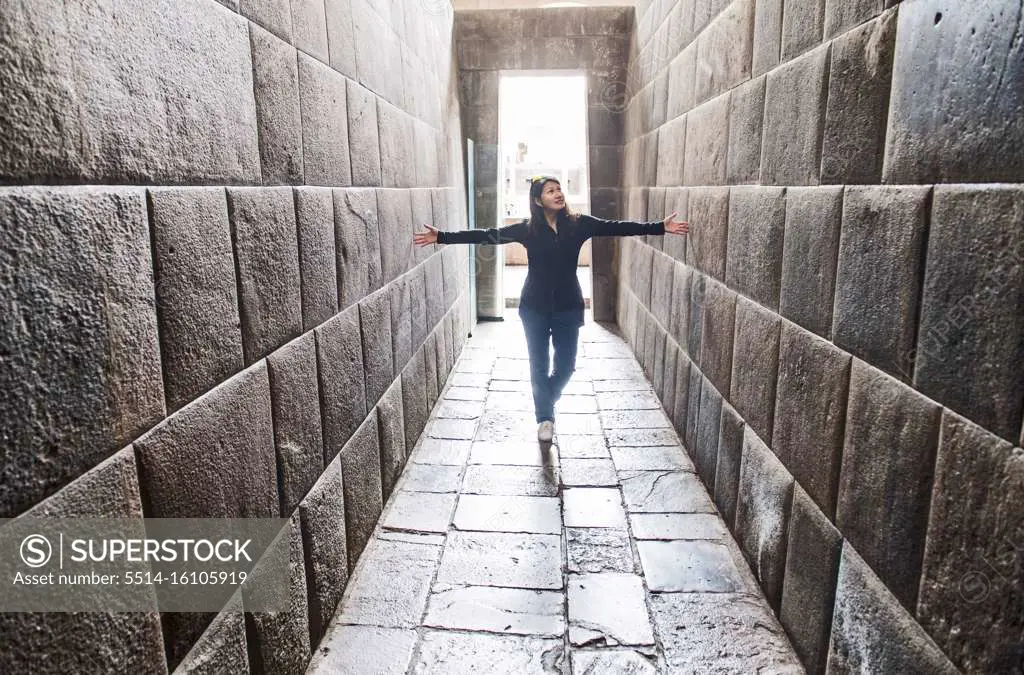 Woman stretching her arms between ancient Inca walls, Cusco, Peru