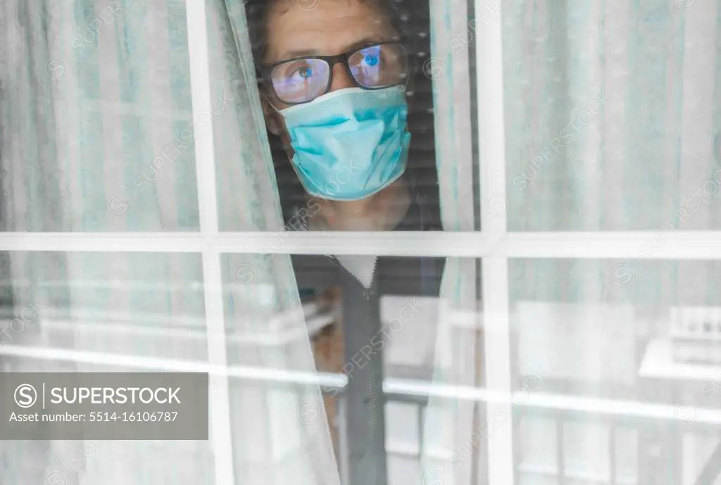 Middle-aged man in the medical mask is quarantined in the hospital and pressed her forehead against the window