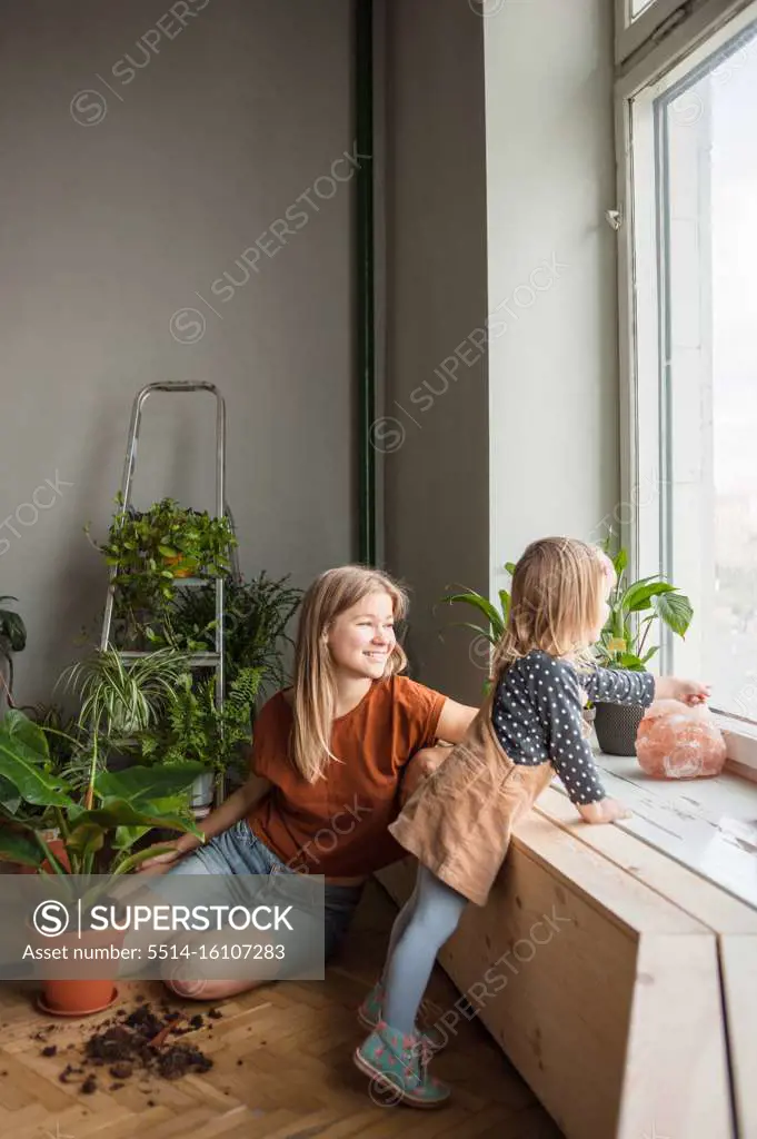 Woman sits and look at window, little girl near points out window.