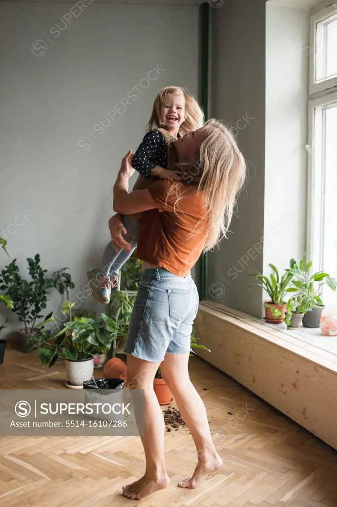 Woman holds in hugs her laughing child in living room with lot plants