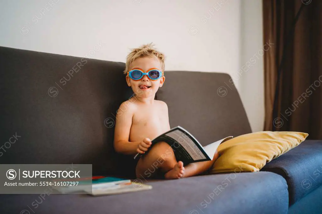 Male child reading topless with goggles and sticking his tongue out