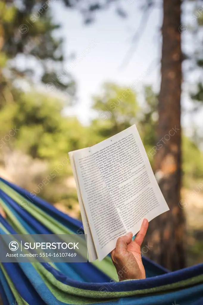 Detail of a hand holding book while someone reads in hammock