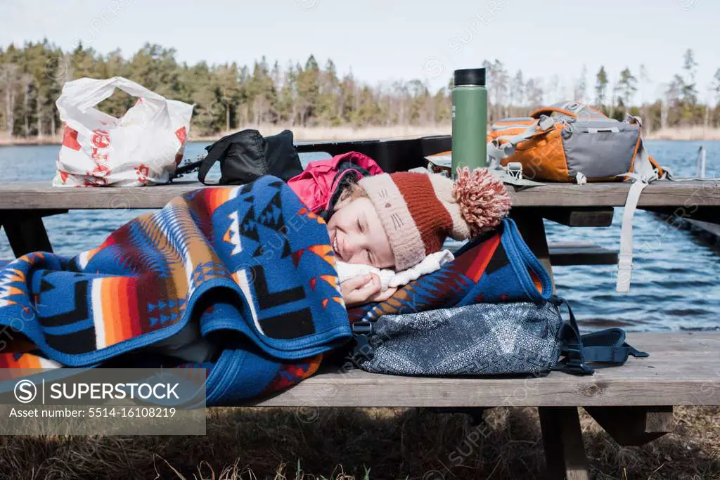 young child laying down on a bench wrapped up in a blanket