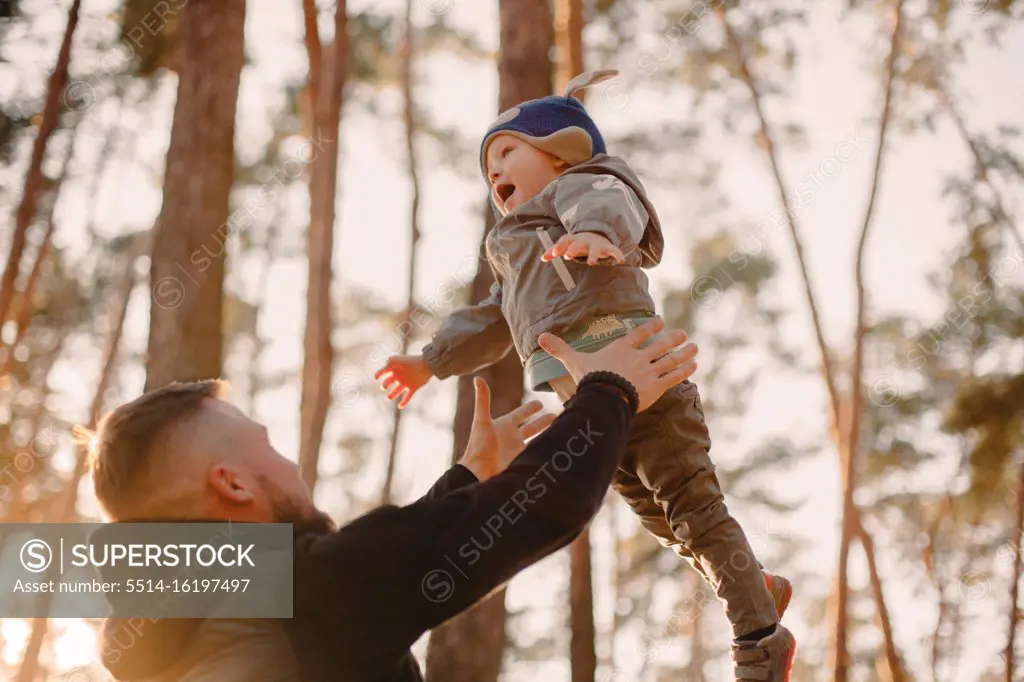 Father throwing son in air while playing in forest