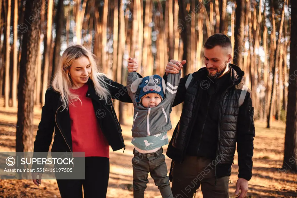 Happy young mother and father holding their child by hands in forest