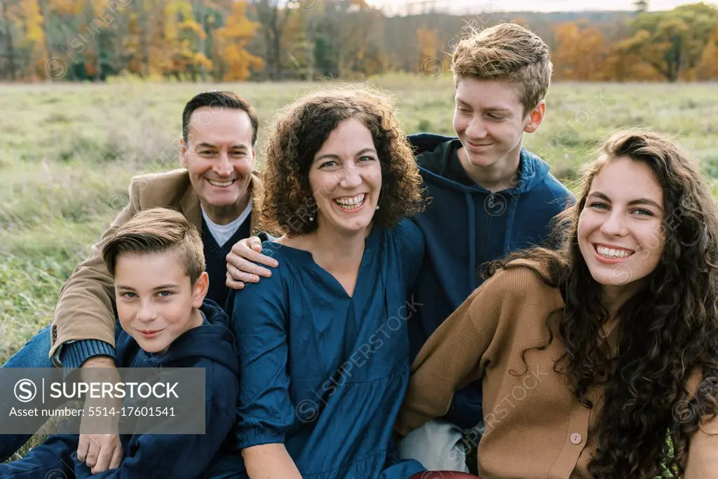 A happy family of five sitting together in a field