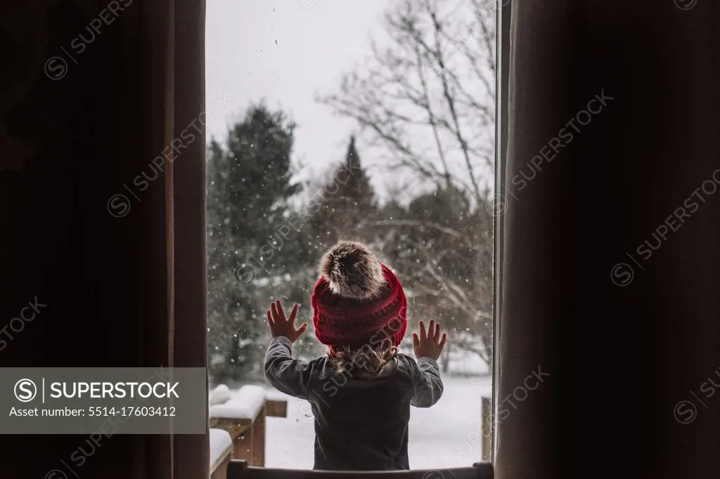 Little girl looks out the window during a snow day in the winter