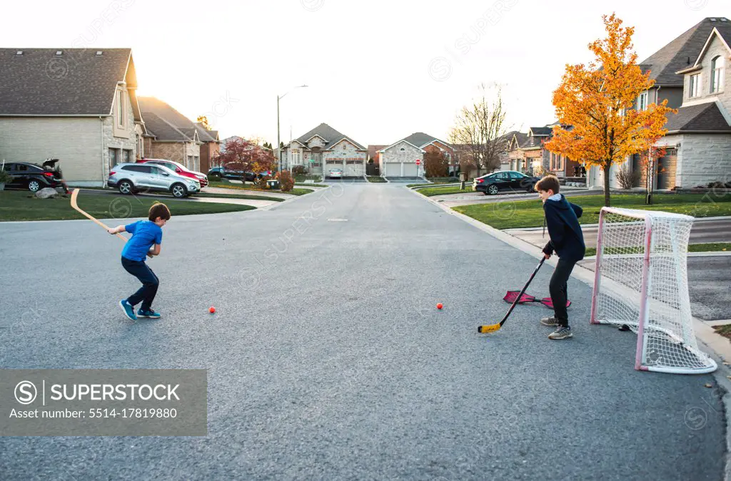 Two boys playing street hockey on a residential street in the fall.