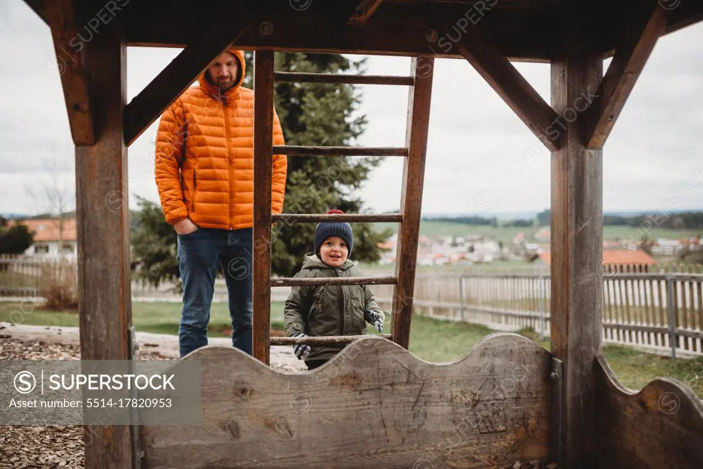 Dad and son at playground in winter climbing ladder to wooden house