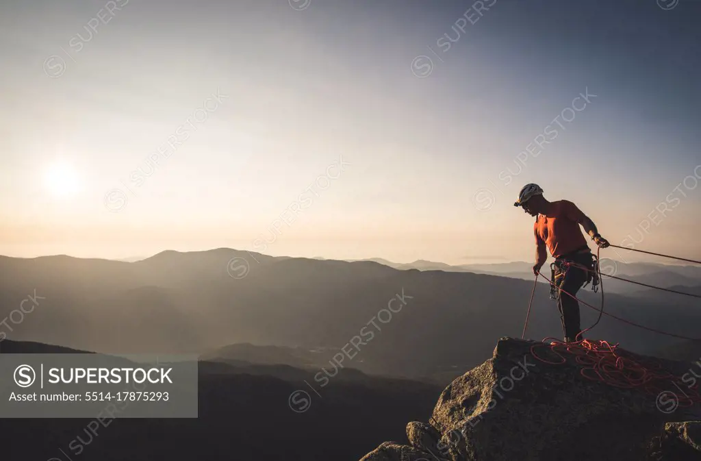 Man belaying with climbng ropes at sunrise in mountains