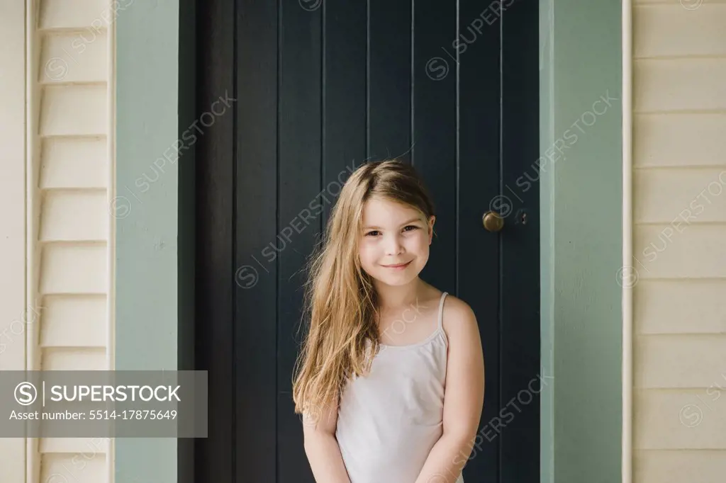 Smiling young girl standing outside in front of a door - SuperStock