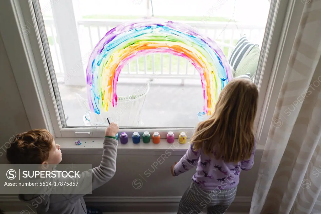 top down view of siblings painting rainbow on living room window