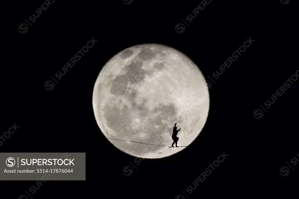 One person walking on a highline in front of the winter full moon