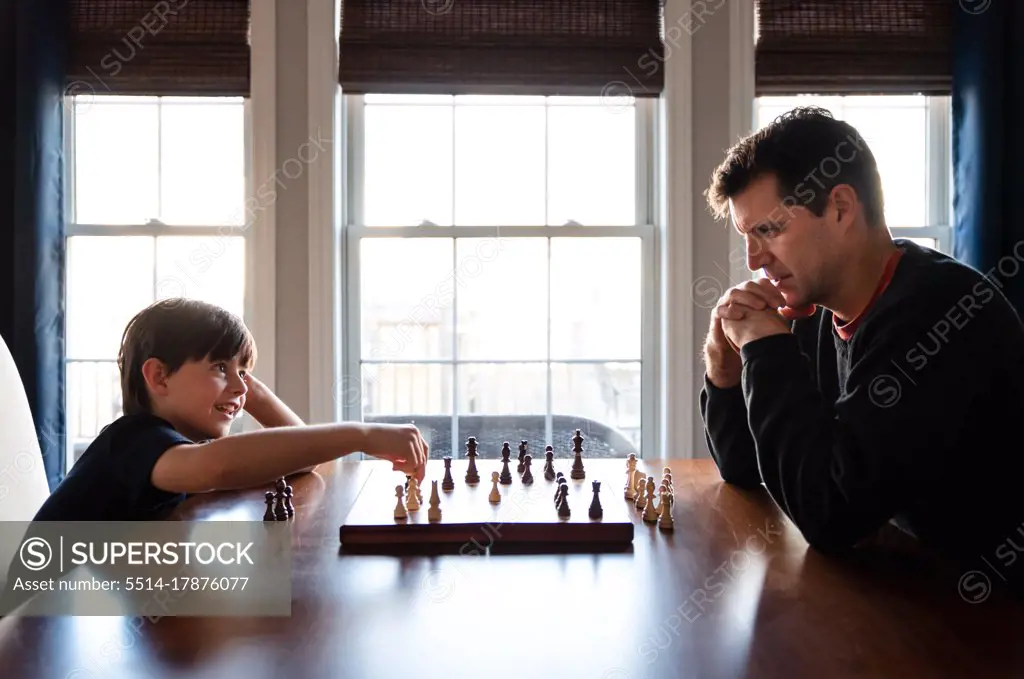 Father and son sitting at a table indoors playing a game of chess.