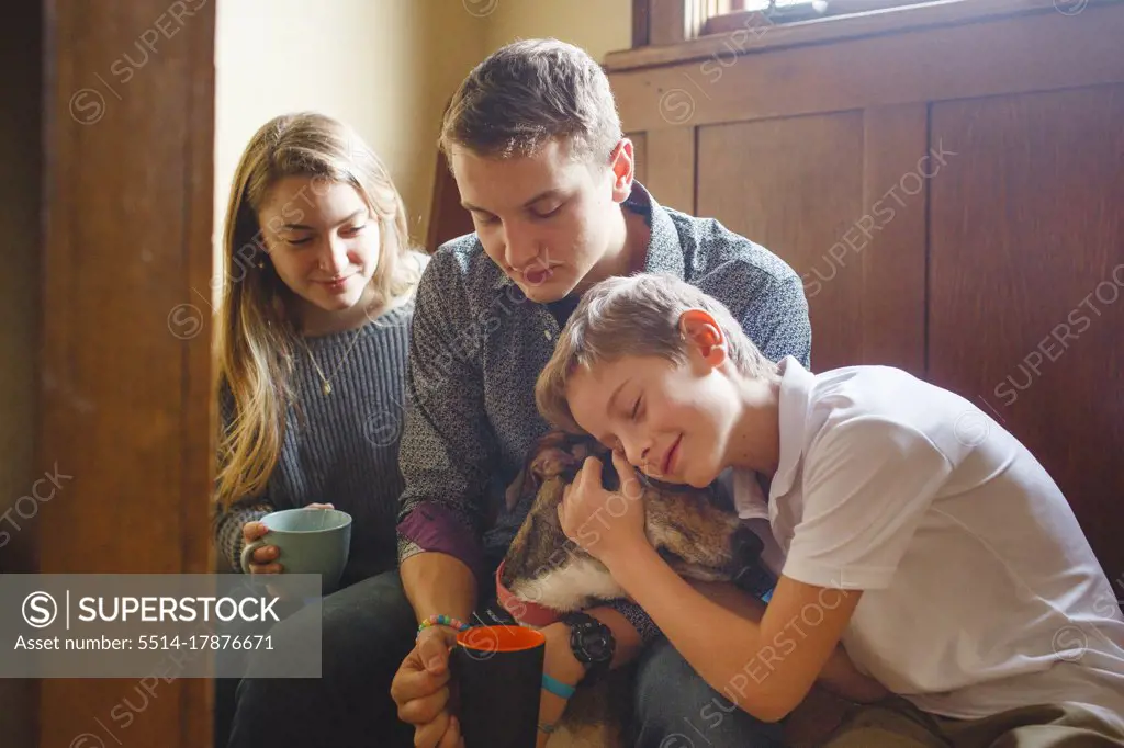 Three happy siblings cuddle their dog in beautiful golden window light